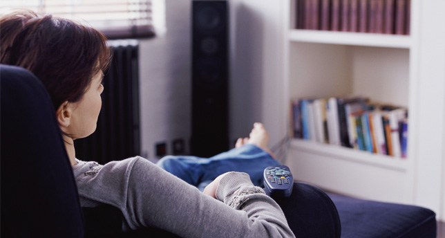 A person sits in a chair, with a TV remote on their leg.