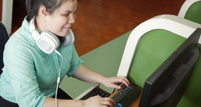 Young blind woman using computer with refreshable Braille display