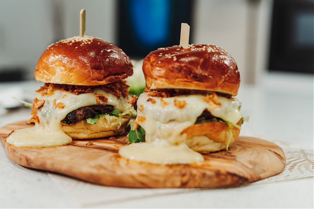 Two Hotzza Mozza Burgers on a wooden cutting board.