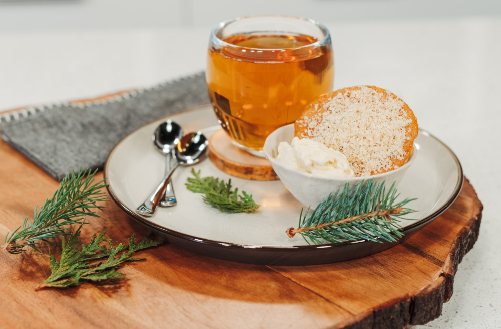 A bowl of ice cream sits on a plate with a glass of cedar tea and ginger snap cookie next to it.